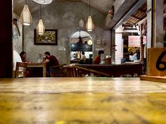 people sitting at tables in a restaurant with lights hanging from the ceiling and wood floors