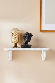 a white shelf topped with a busturine next to a candle holder on top of a wall