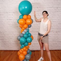 a woman standing in front of a tall balloon column with orange, blue and grey balloons