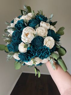 a bridal bouquet with white and teal flowers is held by someone's hand