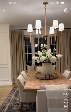 a dining room table with white flowers in a basket on it and two lamps hanging from the ceiling