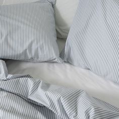 an unmade bed with blue and white striped sheets, pillows and pillowcases