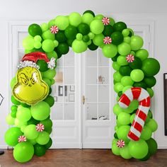 an arch made out of green balloons with the grin face on it and candy canes