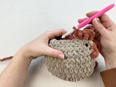 a woman is crocheting a small stuffed animal with a pink pen in her hand