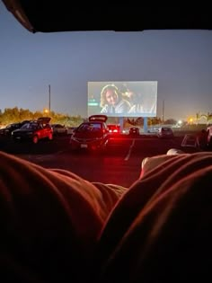 cars parked in a parking lot at night with a movie on the wall behind them