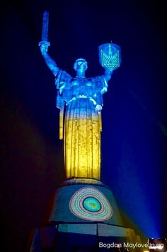 the statue of liberty is lit up in blue and yellow light at night with its arms raised