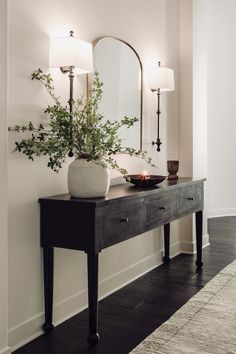 a table with a mirror and vase on it in front of a wall mounted lamp