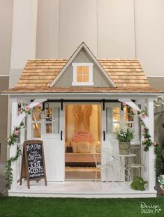 a doll house is set up in the grass with flowers and greenery around it