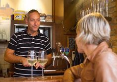 a man standing behind a bar with a glass of wine in front of him and an older woman sitting at the bar