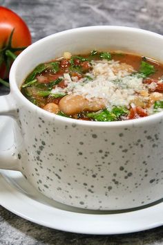 a white bowl filled with soup sitting on top of a plate next to a tomato