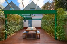 an outdoor dining area with wooden flooring and green canopy over the table, surrounded by greenery