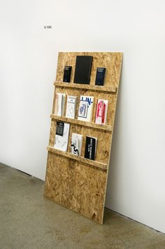 a wooden shelf with books and other items on it next to a white wall in an empty room