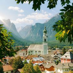 a town with mountains in the background and trees on the foreground, surrounded by greenery