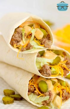 two burritos filled with meat, cheese and pickles on a white plate