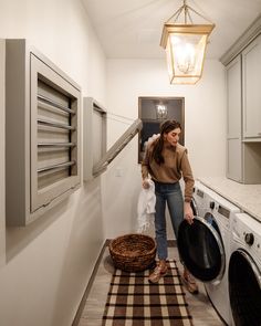 a woman standing next to a washer and dryer in a room with white walls