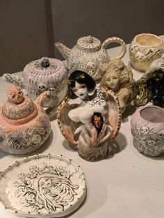 a table topped with lots of different types of vases and dishes on top of a white table cloth