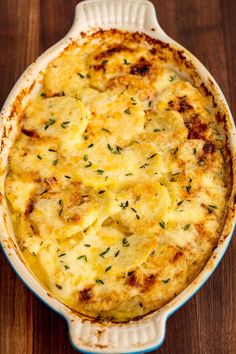 a casserole dish with cheese and herbs in it sitting on a wooden table