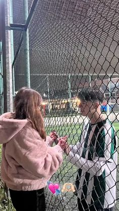 two people standing in front of a chain link fence with candy floss on them