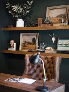 a desk with a chair, lamp and pictures on the shelves in front of it