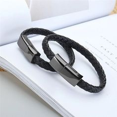 two black leather bracelets with stainless steel clasps on top of an open book