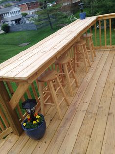 a wooden deck with barstools and stools on the bottom level next to a potted plant