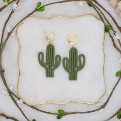 two green cactus shaped earrings sitting on top of a white table next to some branches