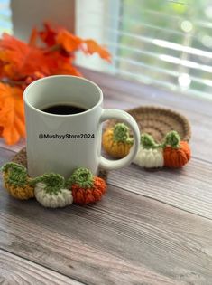 a cup of coffee sitting on top of a table next to some crocheted pumpkins