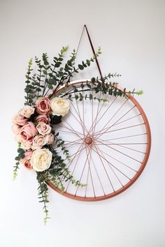 a bicycle wheel with flowers and greenery hanging from it's side on the wall