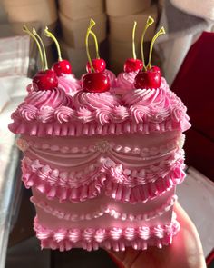 a cake with pink icing and cherries on top is being held by someone