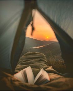 an open tent with the sun setting in the distance, and a book laying on top of it