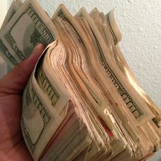 a stack of twenty dollar bills being held by a person's hand in front of a white wall