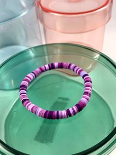 a purple and green bracelet sitting on top of a glass plate next to plastic containers