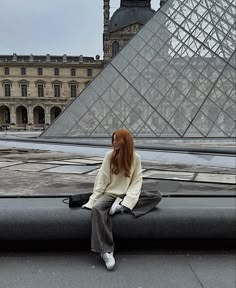 a woman sitting on top of a roof next to a tall building with a pyramid in the background