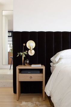 a bedroom with a black headboard, white sheets and a wooden table next to the bed