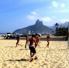 some people are playing soccer on the beach with mountains in the backgrouds