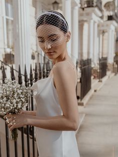 a woman in a white dress holding a bouquet of flowers and wearing a birdcage veil