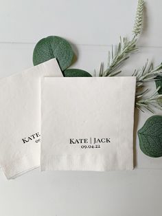 two personalized napkins sitting on top of each other next to some green leaves