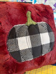 a red pillow with a black and white checkered pumpkin patch on the front, sitting on a cutting board