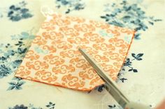 a pair of scissors cutting fabric on top of a flowered tablecloth with blue and orange flowers