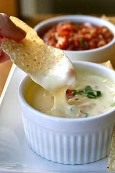 a person dipping tortilla chips into a bowl of dip