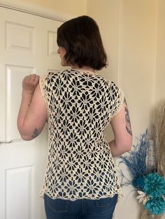 a woman standing in front of a door with her back turned to the camera, wearing a crocheted top