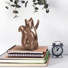 a gold squirrel statue sitting on top of books next to an alarm clock