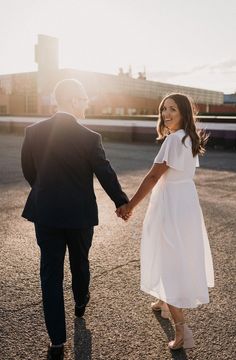 a man and woman holding hands walking down the street