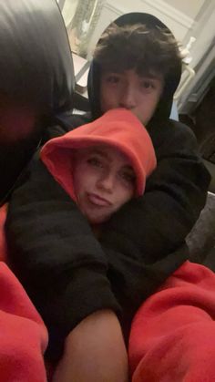 two young men sitting next to each other wearing red and black hoodie sweatshirts