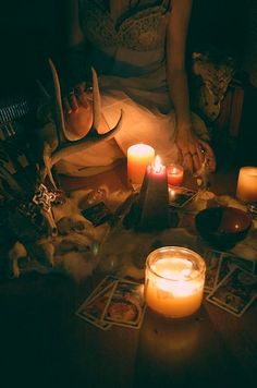 a woman sitting on the floor with candles in front of her and other items around her