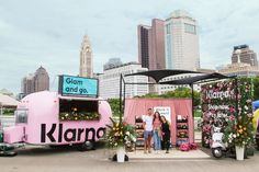 two women standing in front of a food truck with flowers on the side and other vehicles behind it