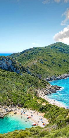 people are on the beach in front of an island with blue water and green hills