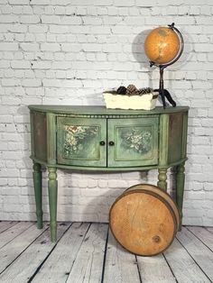 an old green painted table with a basket on it and a globe sitting on top