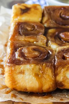 cinnamon rolls sitting on top of wax paper covered in caramel sauce and drizzled with icing