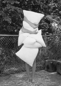 a woman standing in front of a fence with pillows on her head and arms around her body